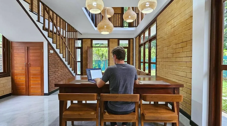 Guest working on a laptop at the villa dining table — Syndeo Garden, Hikkaduwa